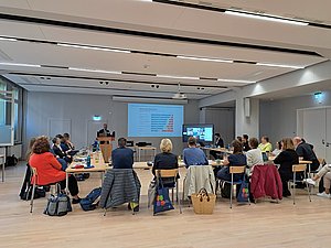 TeilnehmerInnen des Fachtags sitzen an Tischen im U-Form vor dem Vortragenden