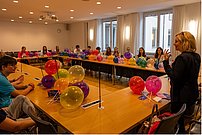 Sprecherin und Zuhörende an Tischkreis mit Luftballons