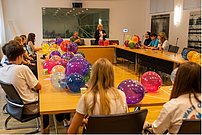 Sprecherin und Zuhörende an Tischkreis mit Luftballons - Ansicht von Hinten